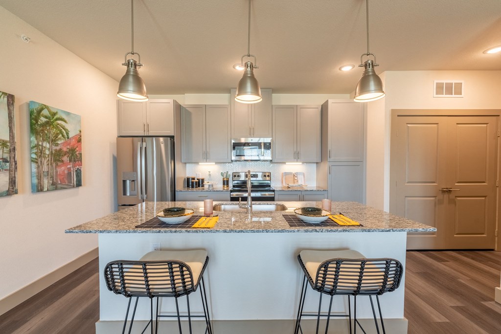 a kitchen with an island and three stools at One Preston Station, Celina, TX, 75009