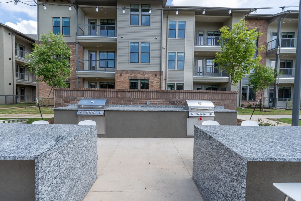 an outdoor barbecue area with two grills at the whispering winds apartments in pearland, tx at One Preston Station, Celina, 75009