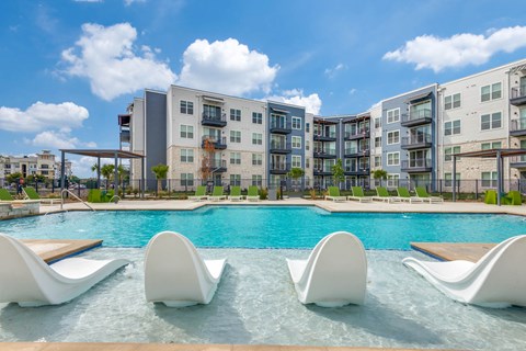A swimming pool with white lounge chairs in front of apartment buildings.