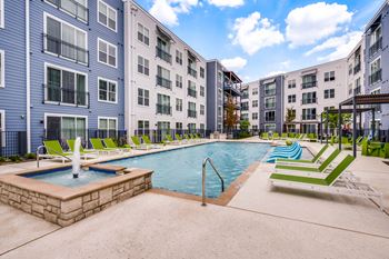 A swimming pool surrounded by lounge chairs and a fountain in a residential area.