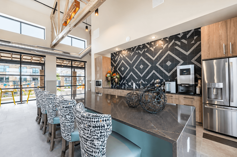 A modern kitchen with a long bar and chairs.