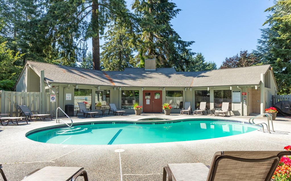 A pool in front of a house with a patio and chairs.