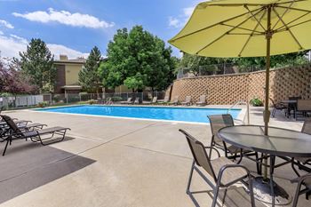 A yellow umbrella is in front of a table and chairs by a pool  at The Buttes Apartments Loveland, CO.