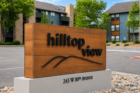 A sign for Hilltop View apartment complex is in front of a parking lot.