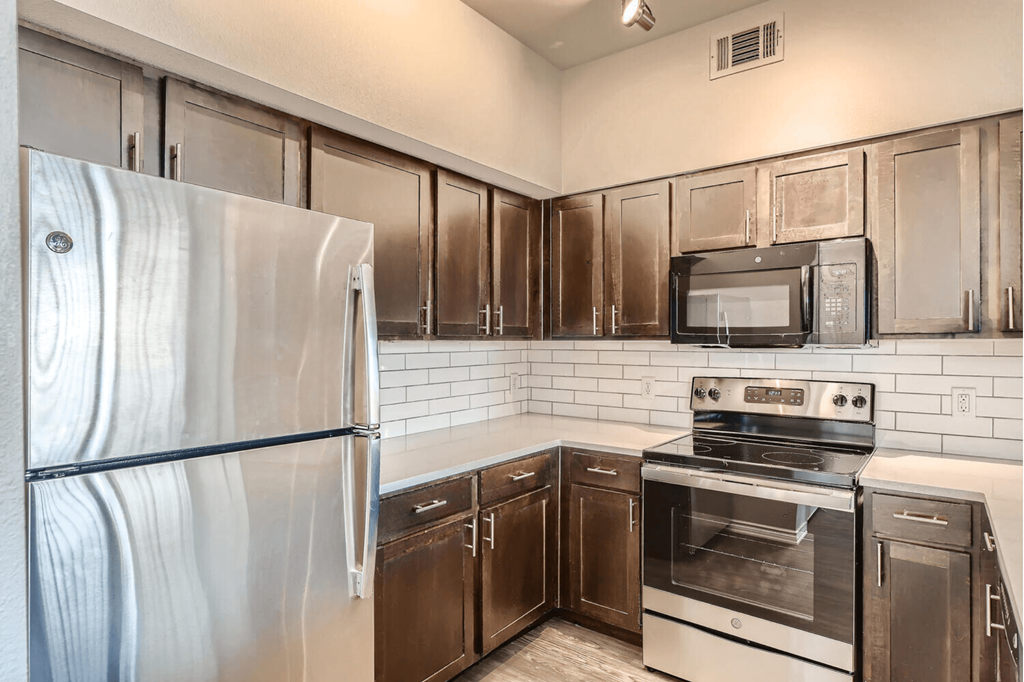 A kitchen with a stainless steel refrigerator, microwave, oven, and cabinets with quartz countertops.