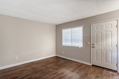 an empty living room with a white door and wooden floors
