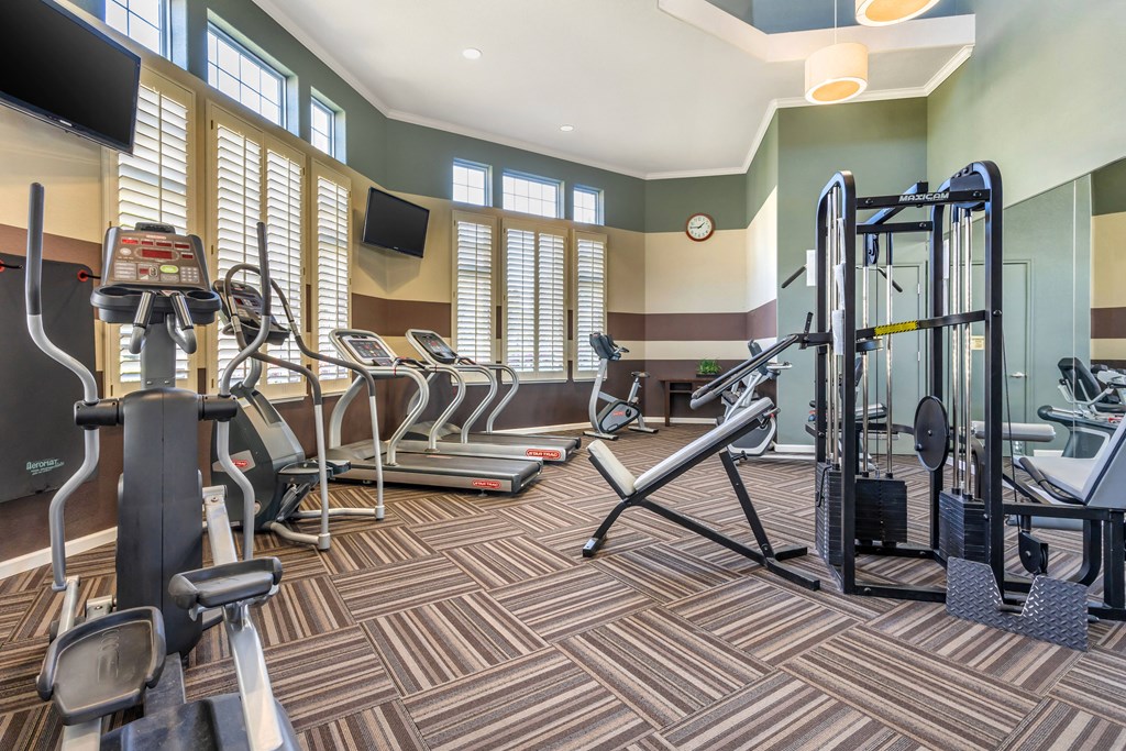 a gym with cardio equipment and weights in a room with windows