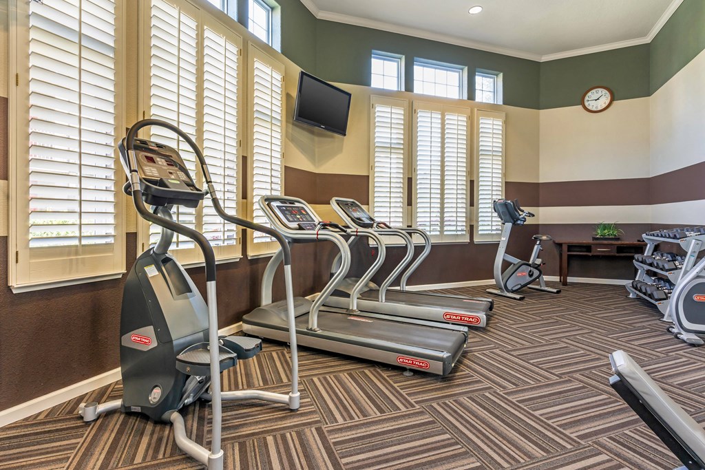 a gym with cardio machines and a tv