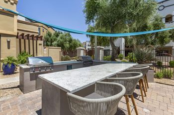 a patio with an outdoor kitchen with a grill and chairs at Trevi Apartment Homes, Chandler, 85224
