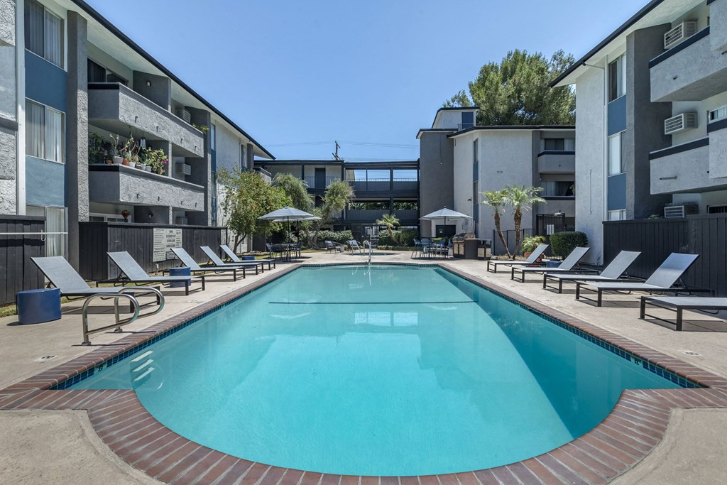 a swimming pool with chaise lounge chairs and umbrellas in front of an apartment building