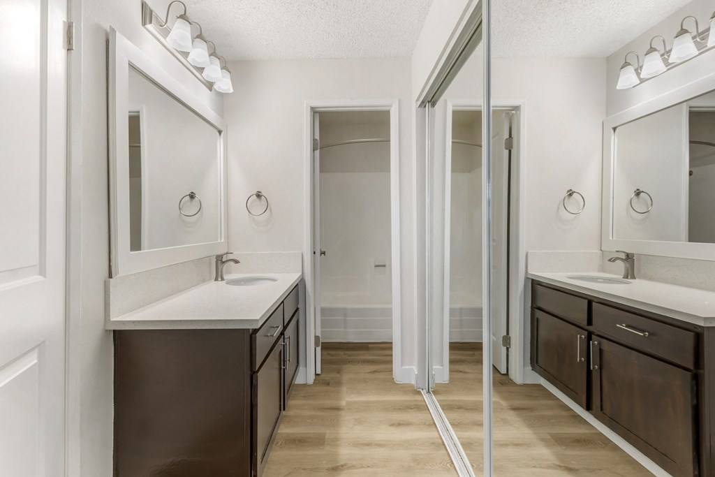This modern bathroom features wide vanities with sleek quartz countertops, framed mirrors, and stylish lighting. A mirrored closet and separate shower area complete the bright, functional space.