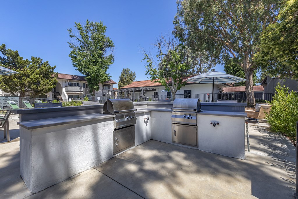 an outdoor kitchen with two grills and a table with chairs and umbrellas at Sage Creek Apartment Homes, Simi Valley California