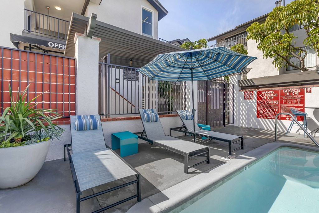 Relaxation meets luxury at Independence Plaza: Your oasis awaits, complete with a serene patio, sparkling pool, and inviting lounge chairs under the shade of a vibrant umbrella.
