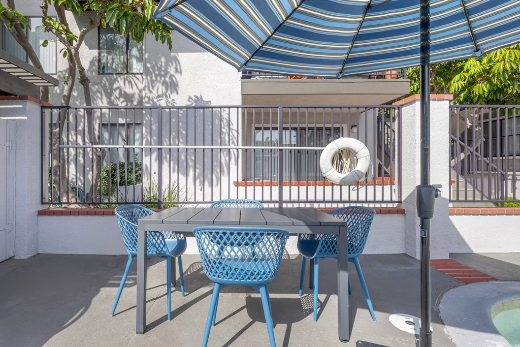 a patio with a table and chRelaxation redefined at Independence Plaza with our updated pool deck, where every moment is a refreshing escape.airs under an umbrella