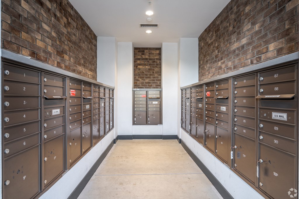 A long hallway with a brick wall and mailboxes on the side.