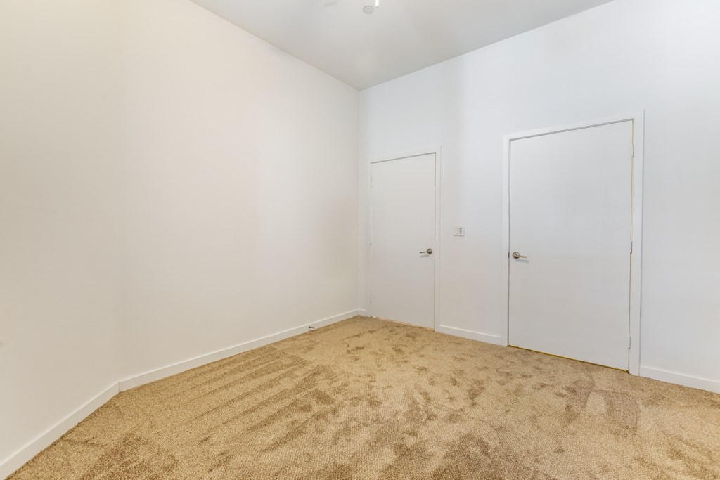 a bedroom with white walls and carpet and two doors at Metro Gateway, Riverside, California