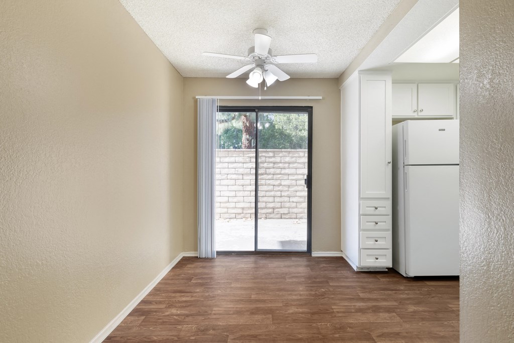 an empty living room with a white refrigerator and a ceiling fan