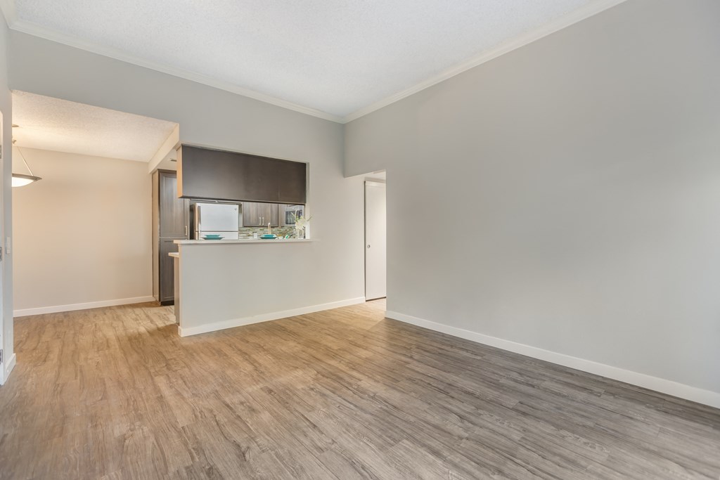 an empty living room with wood flooring and a kitchen