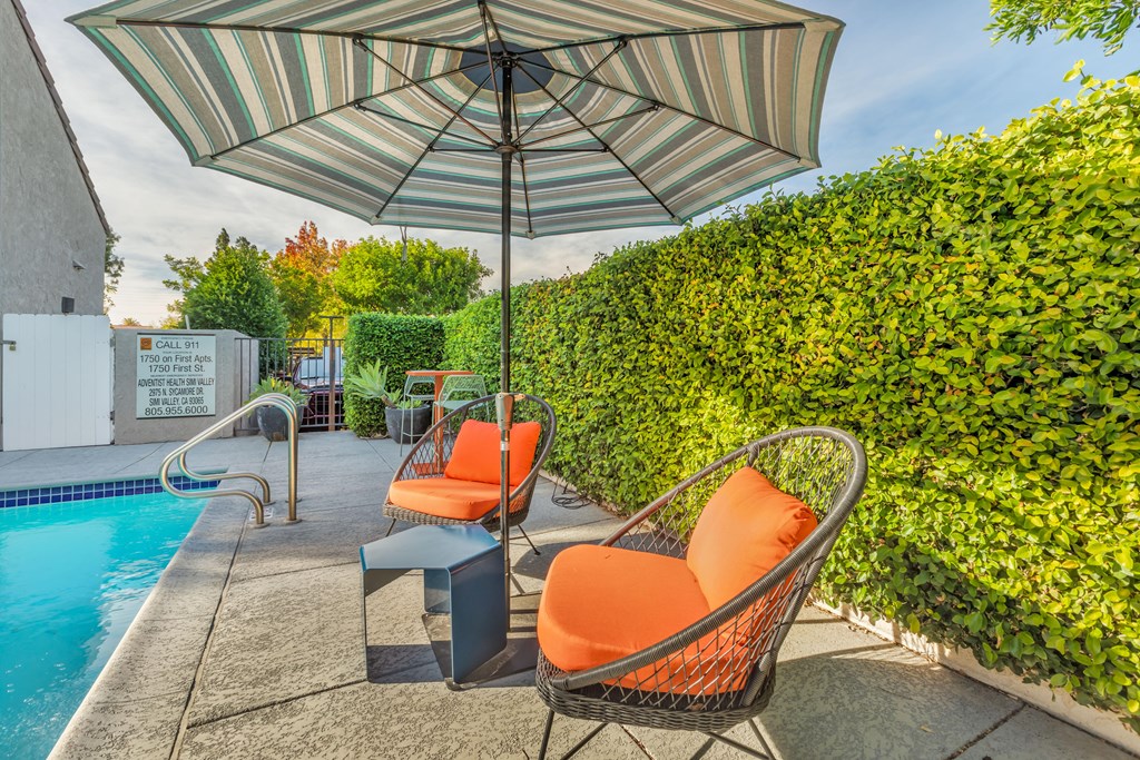 a patio with chairs and an umbrella next to a pool