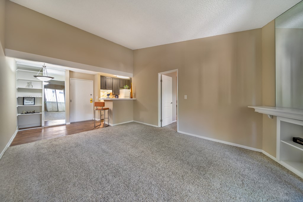 an empty living room with carpet and a kitchen