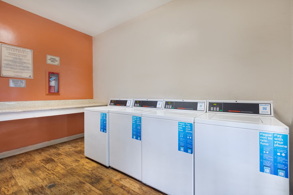 four washers and dryers in a laundry room with orange walls and wooden floors