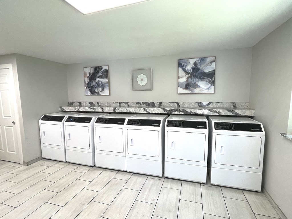 a row of white washers and dryers in a laundry room with a row