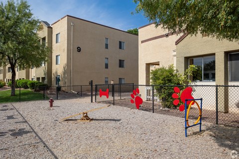 A playground with a seesaw, swings, and climbing frame in front of a building with the number 9 on it.