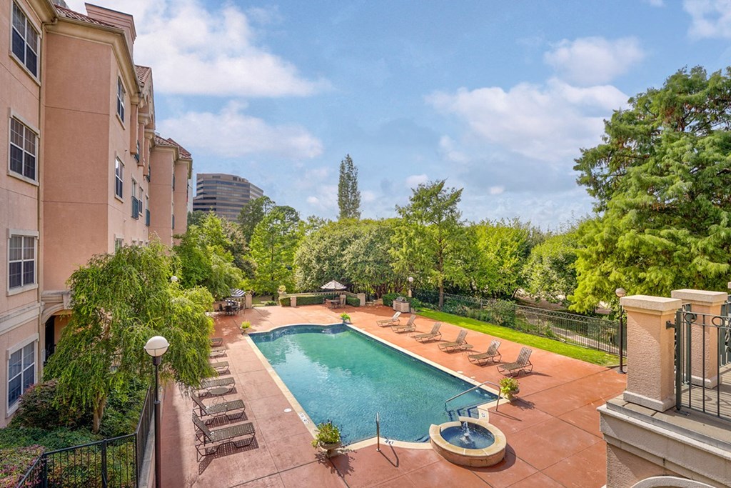 A swimming pool with lounge chairs and a building with trees at Villas at Katy Trail Apartments, Dallas, TX, 75201