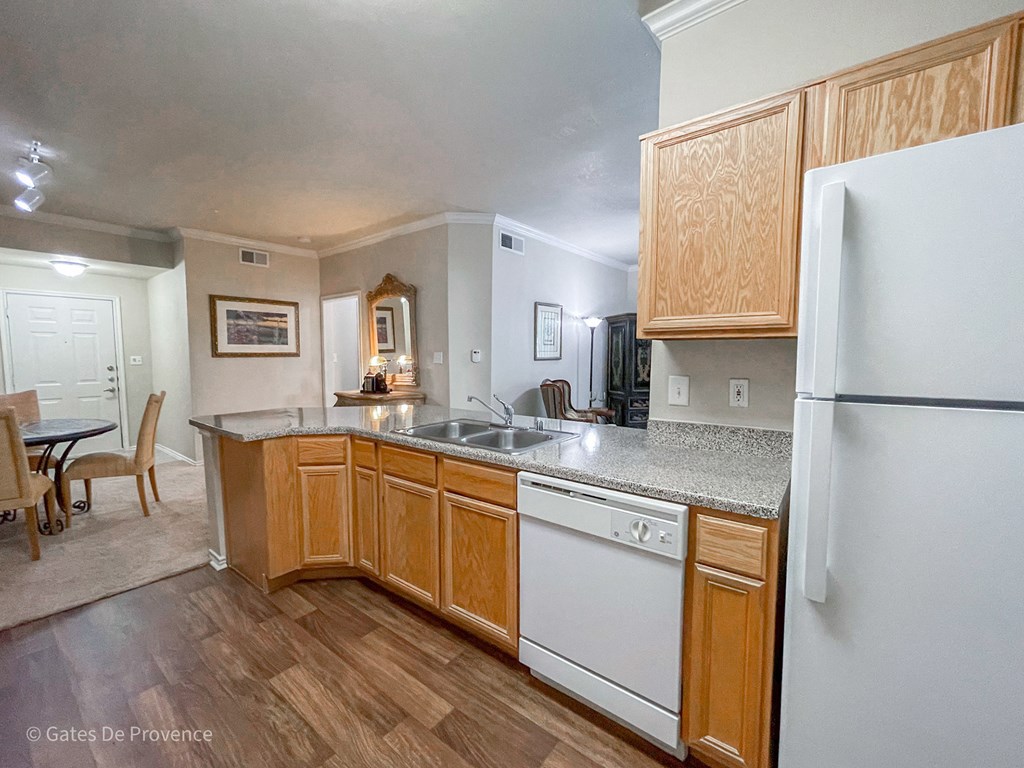 Kitchen view with wooden cabinets and white appliances at Gates de Provence Apartments, Dallas 75287
