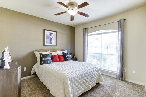 A bedroom with a bed, pillows, a ceiling fan, and a window with curtains.