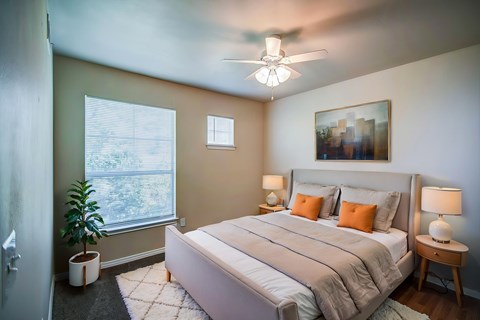 A bedroom with a large bed, a ceiling fan, and a window with blinds.