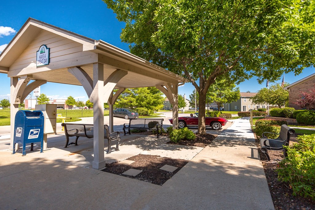 A covered outdoor seating area with a mailbox and a tree at Prairie Commons - 55+ Senior Community Apartments, Lawrence, KS, 66049