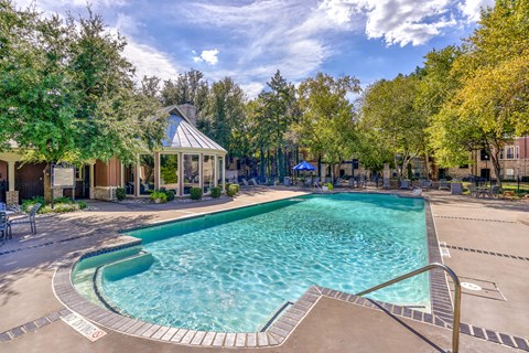 A large outdoor swimming pool surrounded by trees and a gazebo.