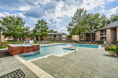 A swimming pool surrounded by a brick wall and a patio area with a bench.