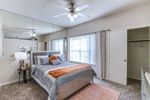 A bedroom with a bed, a ceiling fan, and a mirror.