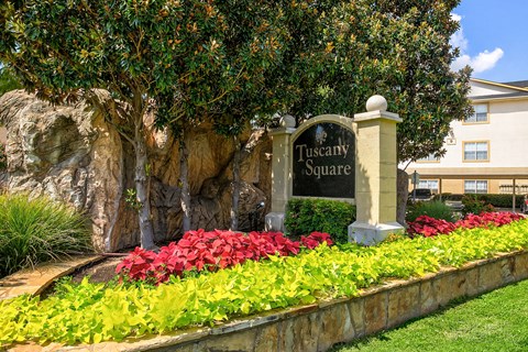 A sign that says Tuscany Square stands in front of a building.