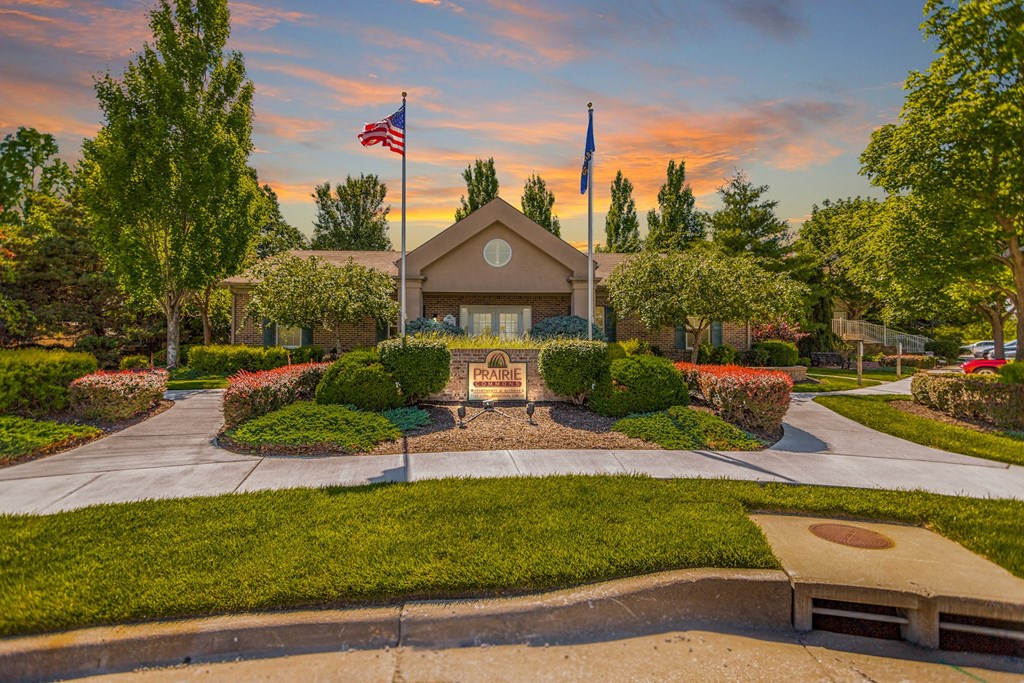 A house with a flag on top of it is surrounded by trees and bushes at Prairie Commons - 55+ Senior Community Apartments, Kansas, 66049