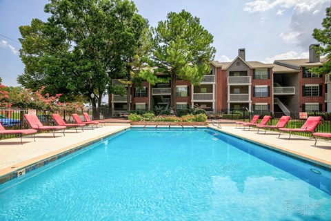A swimming pool surrounded by red chairs and trees.