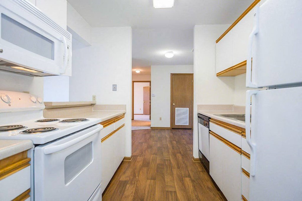 A kitchen with white appliances and wooden floors at Prairie Commons - 55+ Senior Community Apartments, Kansas