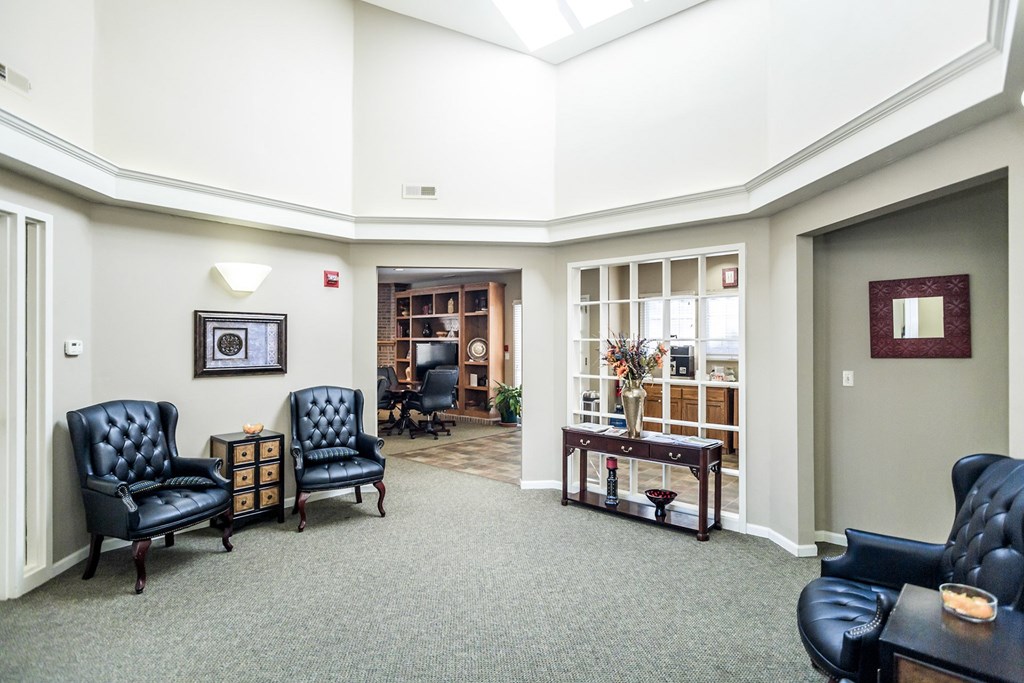 A living room with a grey carpet and black leather chairs at Prairie Commons - 55+ Senior Community Apartments, Kansas