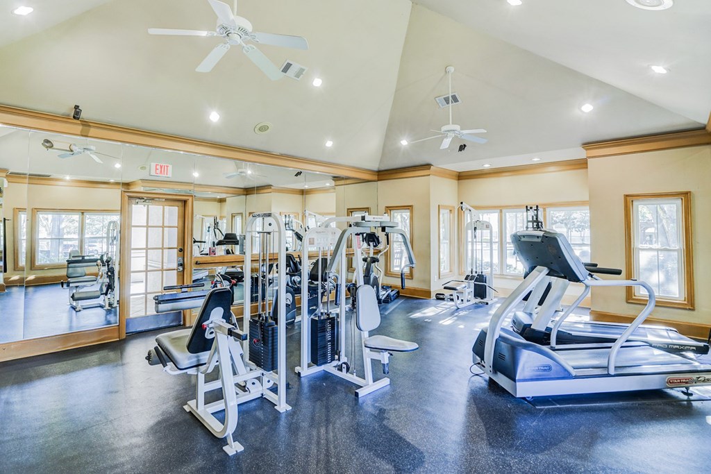 Fully equipped fitness center at Saxony at Chase Oaks Apartments in Dallas, TX, featuring treadmills, weight machines, and mirrored walls in a well-lit space with ceiling fans.