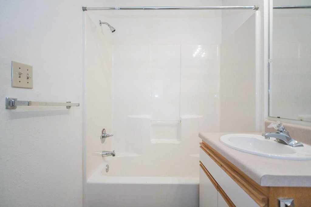 A white bathroom with a tub, sink and mirror at Prairie Commons - 55+ Senior Community Apartments, Lawrence, KS, 66049