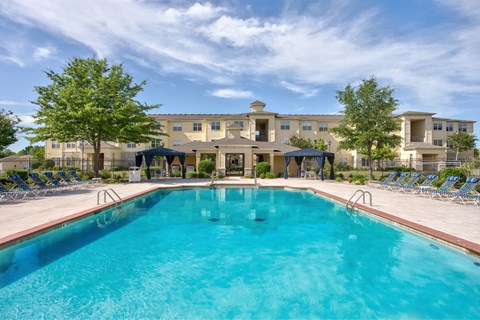 A large swimming pool in front of a building with a blue sky and clouds in the background.