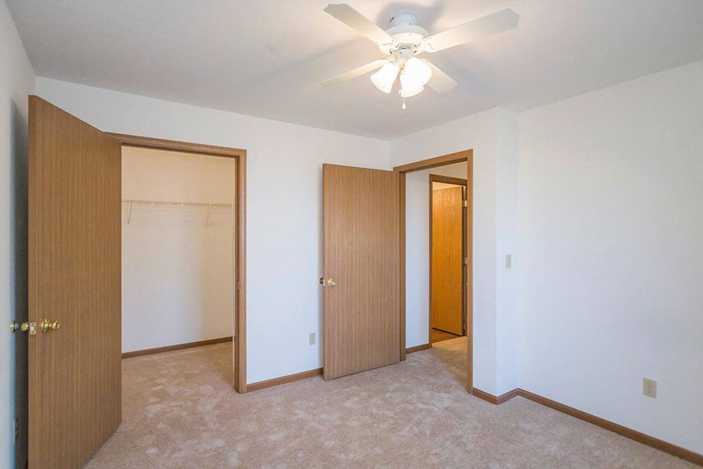A room with a ceiling fan and three doors at Prairie Commons - 55+ Senior Community Apartments, Lawrence