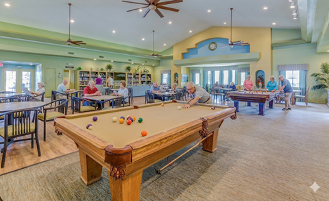 A group of people playing pool in a room with a ceiling fan.