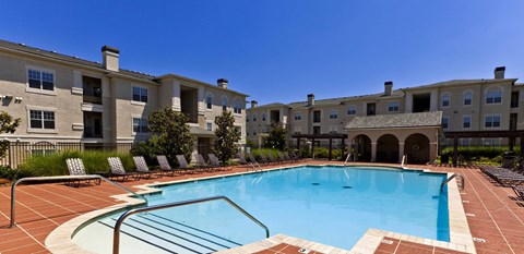 A swimming pool in front of a building with a fence and trees.