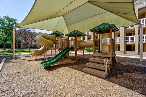 A playground with a green slide and a yellow and green canopy.