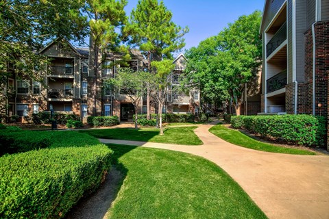 A pathway leads through a grassy area between two apartment buildings.