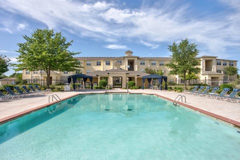A large swimming pool in front of a building with a blue sky and clouds in the background.