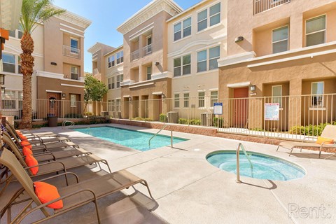 A pool area with sun loungers and a fence in front of apartment buildings.